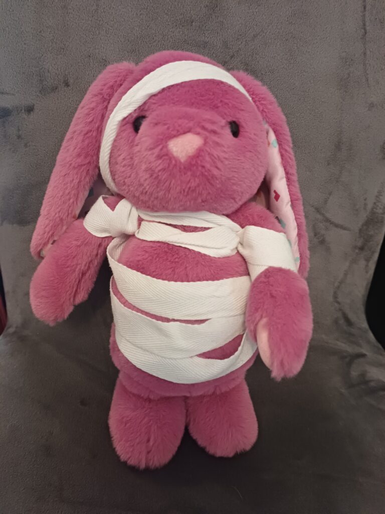 Rosa Plüschhäschen mit einem weißen Band halb und schief eingewickelt. 
